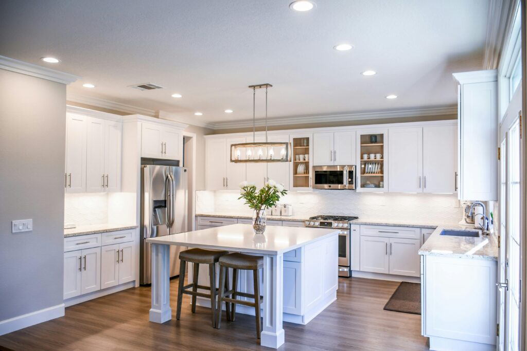 pexels-photo-2724748-2724748 Elegant white kitchen featuring an island, modern appliances, and ample natural light.