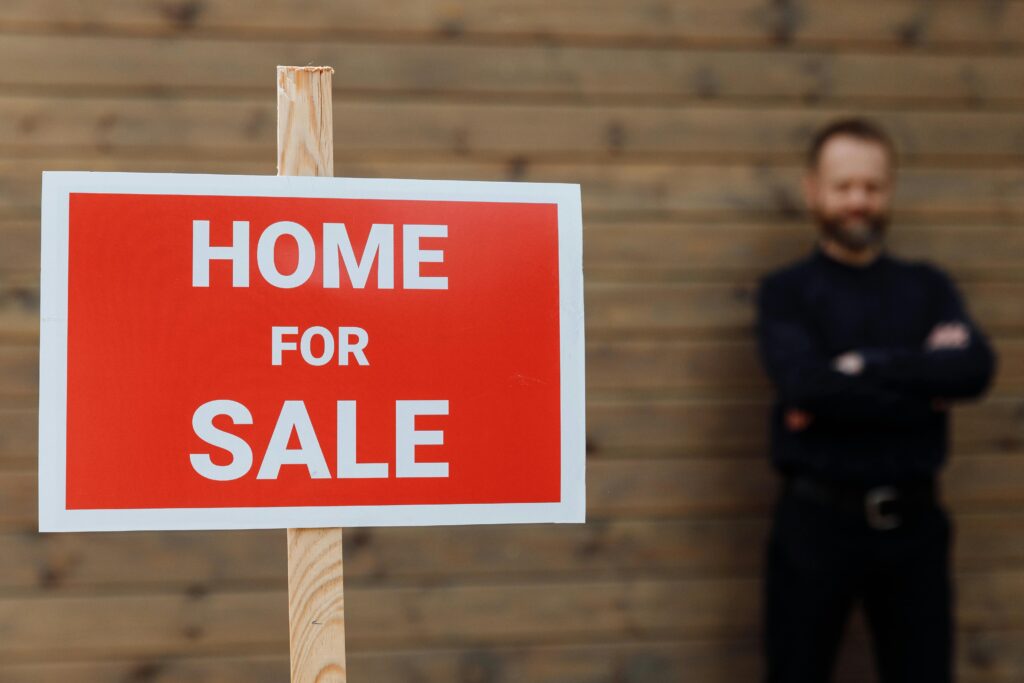 pexels-photo-8482523-8482523 A confident real estate agent stands by a home for sale sign against a wooden wall.